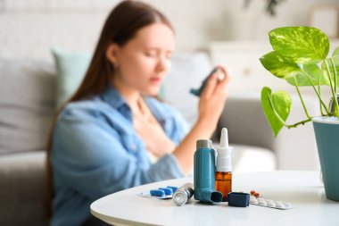 Astım krizi geçiren genç bir kadın yatak odasında modern astım spreyi kullanıyor, ilaç ve ilaçlara odaklanıyor.