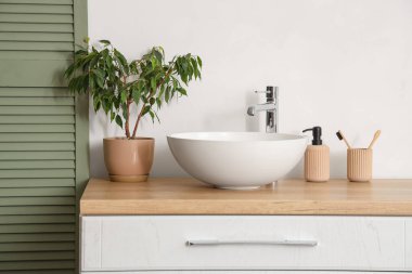 Banyoda beyaz duvarın yanında lavabo, bitki ve banyo malzemeleri olan çekmeceler, yakın plan.