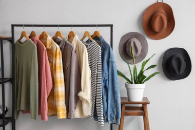 Beyaz duvarın yanında farklı giysiler, dışkı ve çiçek rafları, yakın plan.