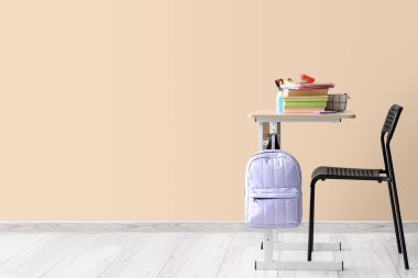 Sırt çantası, kitaplar ve bej arka planı olan modern okul masası.