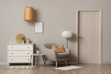 Beyaz çekmeceli rahat bir koltuk ve oturma odasındaki gri duvarın yanında yer lambası.