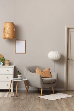 Beyaz çekmeceli rahat bir koltuk ve oturma odasındaki gri duvarın yanında yer lambası.