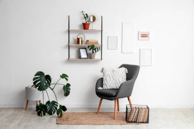 Yumuşak yastıklı rahat gri koltuk ve oturma odasındaki beyaz duvarda asılı raflar.