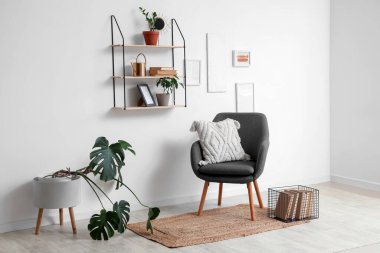 Yumuşak yastıklı rahat gri koltuk ve oturma odasındaki beyaz duvarda asılı raflar.