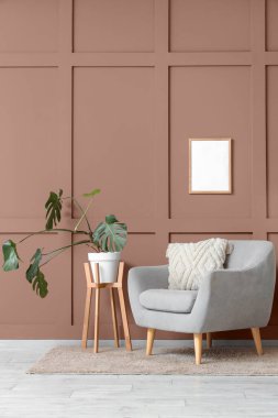 Yumuşak yastıklı rahat gri koltuk ve oturma odasındaki kahverengi duvarın yanındaki bitki örtüsü.