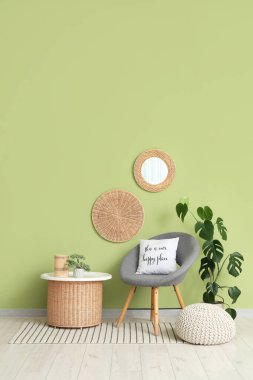 Oturma odasındaki yeşil duvarın yanında yumuşak puf ve masa olan rahat gri koltuk.