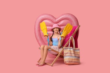 Yüzgeçli ve şişme şilteli şirin kız pembe arka planda iskemlede oturuyor.