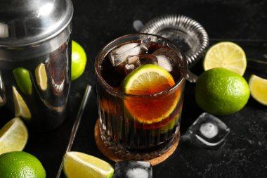 Bir bardak soğuk Küba kokteyli ve siyah arka planda limon, yakın plan.