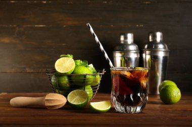 Bir bardak soğuk Küba Libre kokteyli ve ahşap kaplama limonlu sepet.