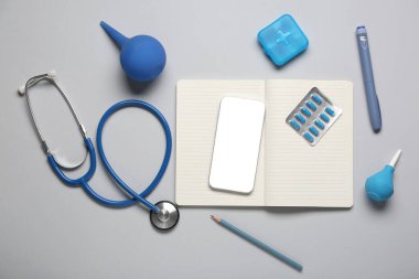 Gri arka planda defter, lavman, hap ve steteskoplu modern cep telefonu.