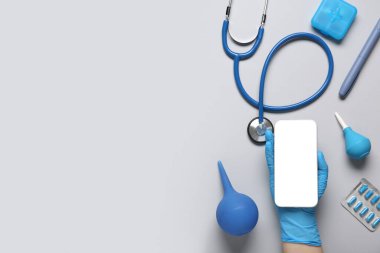 Gri arka planda modern cep telefonu, lavman, hap ve steteskop ile doktor eli.