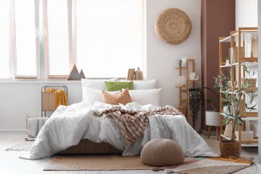 Konforlu yatağı ve pencerenin yanındaki raf ünitesi olan aydınlık yatak odası.