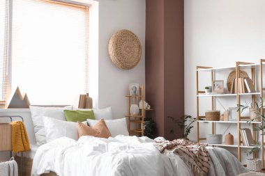 Konforlu yatağı ve pencerenin yanındaki raf ünitesi olan aydınlık yatak odası.