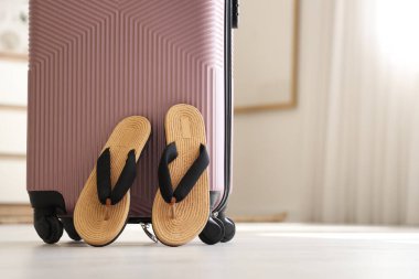 Bavul ve şık terlikler otel odasında yerde.