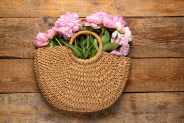 Ahşap arka planda pembe şakayık çiçekleri olan hasır çanta.