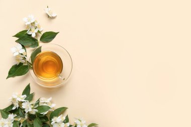 Bej arkaplanda çiçekler olan bir bardak sıcak yasemin çayı.