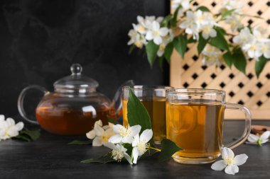 Cam bardaklar ve bir çaydanlık sıcak yasemin çayı. Siyah arka planda çiçekler.