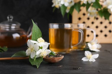 Bir bardak sıcak yasemin çayı, çiçekler ve siyah arka planda kuru yapraklar.