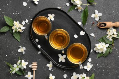 Bir bardak sıcak yasemin çayı, çiçekler ve siyah arka planda kuru yapraklar.