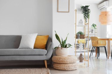 Beyaz duvarın yanında rahat gri kanepesi, pufları ve çiçekleri olan şık bir oturma odası.