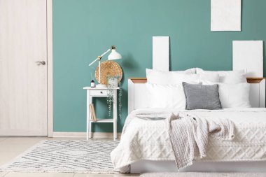 Yatak odasındaki yeşil duvarın yanında büyük, rahat bir yatak ve komodinin yanında.