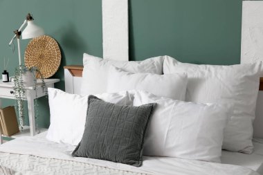 Yatak odasındaki yeşil duvarın yanında büyük, rahat bir yatak ve komodinin yanında.