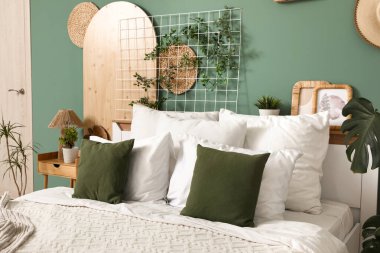 Büyük, rahat bir yatak, komodin ve yatak odasındaki yeşil duvarın yanındaki bitkiler.