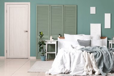 Büyük rahat bir yatak, katlanır ekran ve yeşil duvarın yanındaki yatak odası.