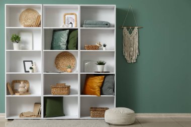 Odanın içinde raf ünitesi ve yeşil duvarın yanında puf var.