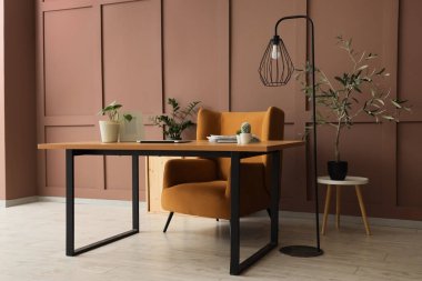 Masası, lambası ve kahverengi duvarı olan rahat bir iş yeri.