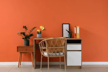 Ofiste turuncu duvarın yanında fotoğraf çerçevesi ve ev bitkileriyle rahat bir iş yeri.