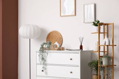 Çekmeceler, raf ünitesi ve zemin lambası. Odanın iç tarafındaki beyaz duvarın yanında. Yakın plan.