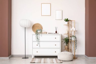 Çekmeceler, zemin lambası, raf ünitesi ve odanın içindeki beyaz duvarın yanında puf.