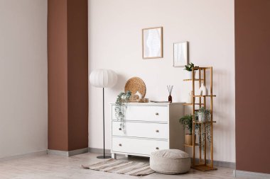 Çekmeceler, zemin lambası, raf ünitesi ve odanın içindeki beyaz duvarın yanında puf.