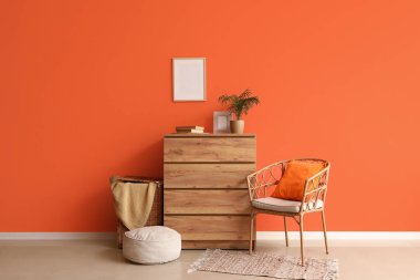 Çekmeceler, çamaşır sepeti ve içi turuncu duvarın yanında puf.