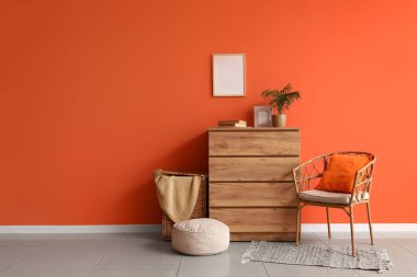 Çekmeceler, çamaşır sepeti ve içi turuncu duvarın yanında puf.