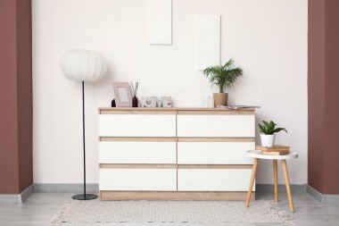 Çekmeceler, masa ve zemin lambası. Odanın içindeki beyaz duvarın yanında.