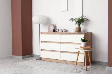 Çekmeceler, masa ve zemin lambası. Odanın içindeki beyaz duvarın yanında.