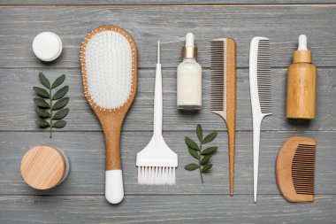 Gri ahşap arka planda saç fırçası, tarak, kavanoz ve kozmetik ürünler içeren kompozisyon
