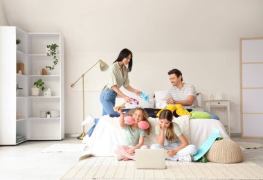 Yatak odasında dizüstü bilgisayarlı bavulları olan turist ailesi.