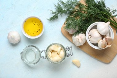 Taze sarımsaklı kavanoz ve açık mavi arka planda bir kase yağ.