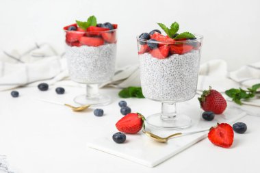 Bardaklar dolusu taze meyveli Chia tohumu pudingi ve beyaz arkaplanda nane şekeri.