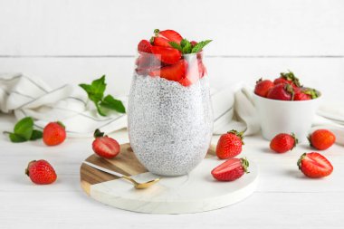 Bir bardak taze çilekli Chia tohumu pudingi ve beyaz ahşap arka planda nane şekeri.