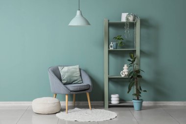 Oturma odasının içindeki nane duvarının yanında rahat koltuk, puf ve raf ünitesi.