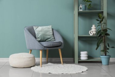 Oturma odasındaki nane duvarının yanında rahat koltuk, puf ve raf ünitesi, yakın plan.