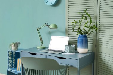 Modern dizüstü bilgisayarı, lambası ve vazosu olan yeşil dalları olan rahat bir iş yeri, yakın plan.