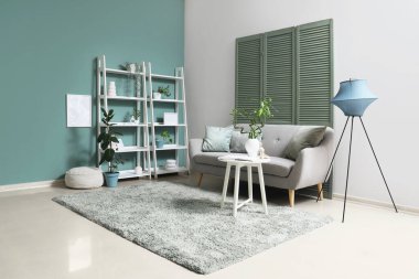 Rahat kanepesi, masası, lambası ve raf ünitesi olan oturma odasının içinde.