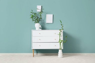 Nane duvarına yakın yeşil dalları olan çekmeceleri ve vazoları olan modern oturma odasının içinde.