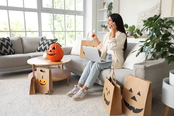 Evde Cadılar Bayramı için kredi kartı alışverişi yapan genç bir kadın.