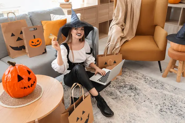 Cadılar Bayramı için giyinmiş genç bir kadın. Cadı kredi kartı ve laptop alışverişi yapıyor.